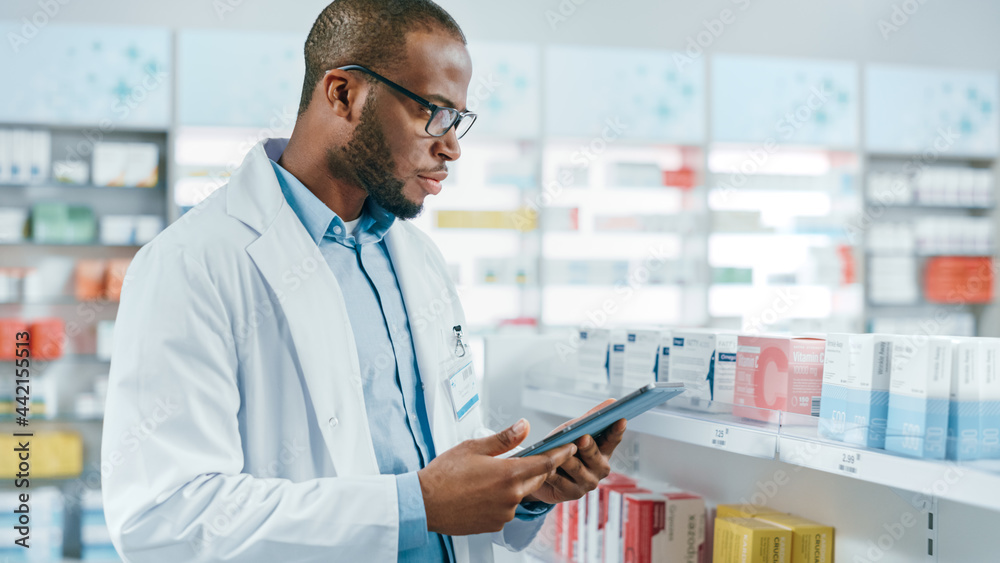 Pharmacy: Portrait of Professional Black Pharmacist Uses Digital Tablet Computer, Checks Inventory of Medicine, Drugs, Vitamins on a Shelf. Drugstore Store Arranging Health Care Products.
