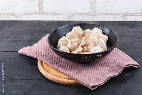 Cooked dumplings in a black round tarek sprinkled with hot pepper on a wooden background photo