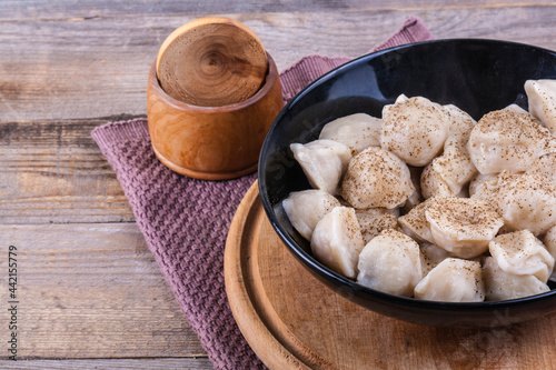 Cooked dumplings in a black round tarek sprinkled with hot pepper on a wooden background photo