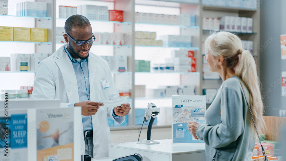 Pharmacy Drugstore Checkout Counter: Black Male Pharmacist Explains Use and Manual for Prescription Medicine Beautiful, Senior Female Customer Paying Using Contactless Credit Card to Terminal