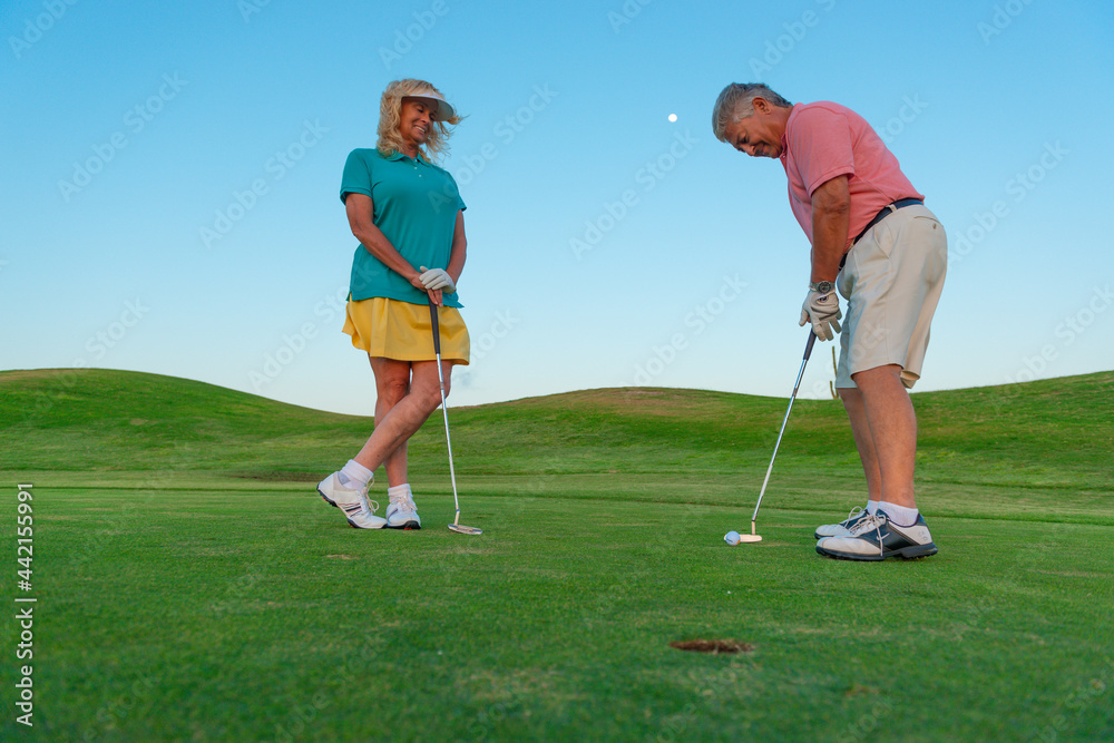 Active senior couple playing golf at sunset at the putting green. Active senior couple playing golf at sunset at the putting green.