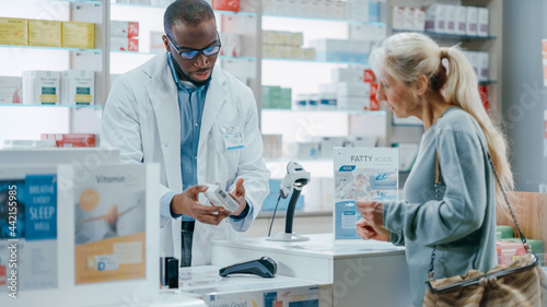 Pharmacy Drugstore Checkout Counter  Black Male Pharmacist Explains Use and Manual for Prescription Medicine Beautiful  Senior Female Customer Paying Using Contactless Credit Card to Terminal