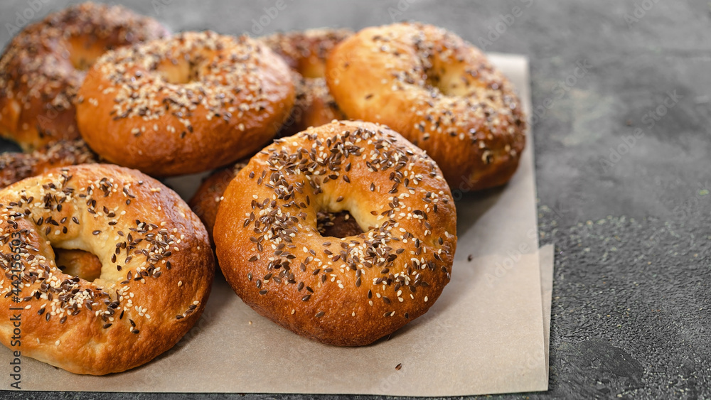 Food banner. Appetizing and crunchy New York bagels with sesame and flax seeds. Homemade hot baked goods. Bagels on baking paper on a gray concrete background. Cook at home. Copy space