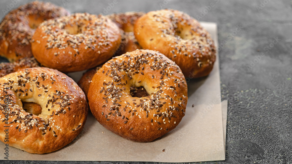 Food banner. Appetizing and crunchy New York bagels with sesame and flax seeds. Homemade hot baked goods. Bagels on baking paper on a gray concrete background. Cook at home. Copy space Food banner. Appetizing and crunchy New York bagels with sesame and flax seeds. Homemade hot baked goods. Bagels on baking paper on a gray concrete background. Cook at home. Copy space