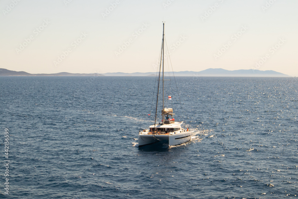 Double-decked catamaran, a yacht with lowered sails, looking towards the horizon. The azure ocean on a sunny day off the coast of Croatia