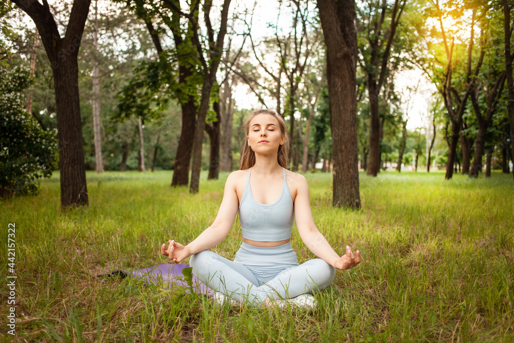 A beautiful woman doing yoga in the park on the grass. Gymnastic mat, sports equipment. Workout, outdoor. Healthy lifestyle, weight loss, fitness. Trained muscular body. Fresh air. sunny glare A beautiful woman doing yoga in the park on the grass. Gymnastic mat, sports equipment. Workout, outdoor. Healthy lifestyle, weight loss, fitness. Trained muscular body. Fresh air. sunny glare