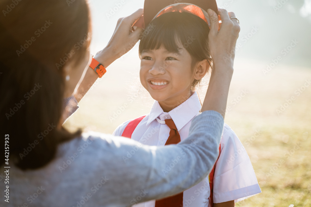 mother fixing her daughter primary school student uniform when take the kid to school. put hat on mother fixing her daughter primary school student uniform when take the kid to school. put hat on