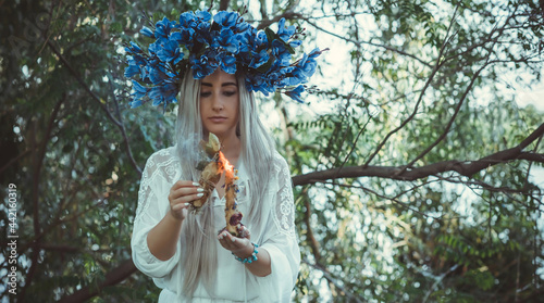 Beautiful girl in wreath of flowers in forest. Portrait of Young beautiful woman wearing white bride dress. Young pagan Slavic girl conduct ceremony on Midsummer. Earth Day