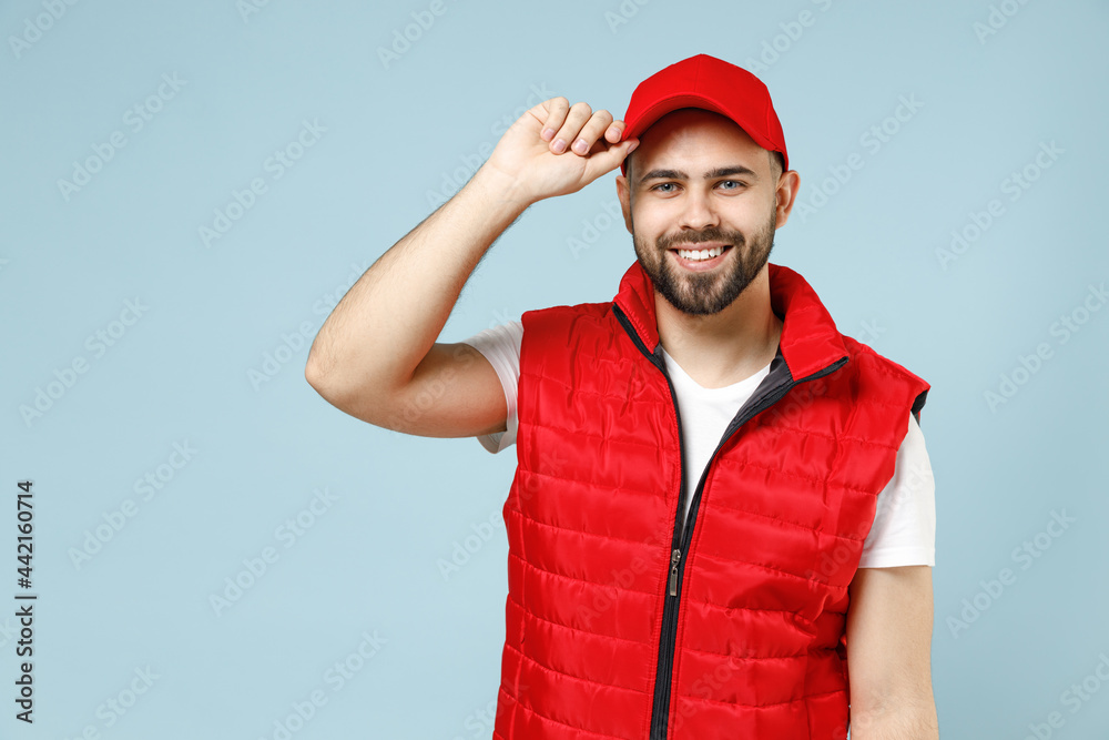 Professional happy delivery guy employee man in white T-shirt vest uniform workwear work as dealer courier hold touch red cap isolated on pastel blue color background studio portrait. Service concept. Professional happy delivery guy employee man in white T-shirt vest uniform workwear work as dealer courier hold touch red cap isolated on pastel blue color background studio portrait. Service concept.