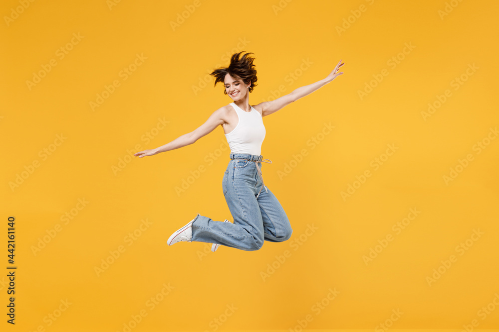 Full length young fun happy overjoyed woman 20s with bob haircut wearing white tank top shirt jumping high with outstretched hands like flying isolated on yellow background People lifestyle concept Full length young fun happy overjoyed woman 20s with bob haircut wearing white tank top shirt jumping high with outstretched hands like flying isolated on yellow background People lifestyle concept
