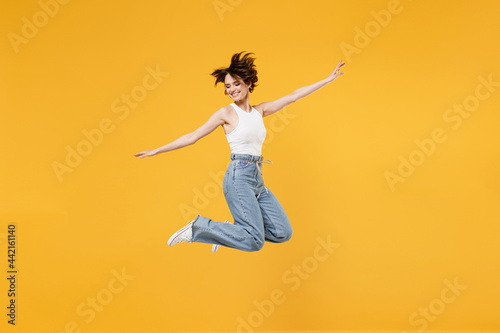 Full length young fun happy overjoyed woman 20s with bob haircut wearing white tank top shirt jumping high with outstretched hands like flying isolated on yellow background People lifestyle concept