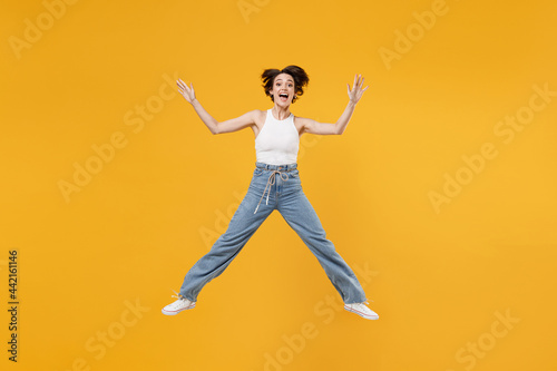 Full length young successful fun overjoyed happy woman 20s with bob haircut wearing white tank top shirt jumping high with outstretched hands isolated on yellow background People lifestyle concept