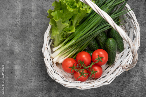 vegetables in a basket on a dark stone background. lettuse, scallion, cucumbers and tomatoes photo