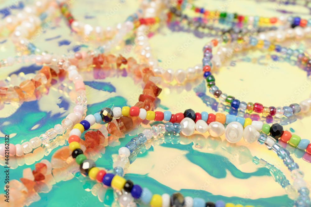 Closeup of necklaces and bracelets made from colorful beads and pearls on a turquoise holographic background.