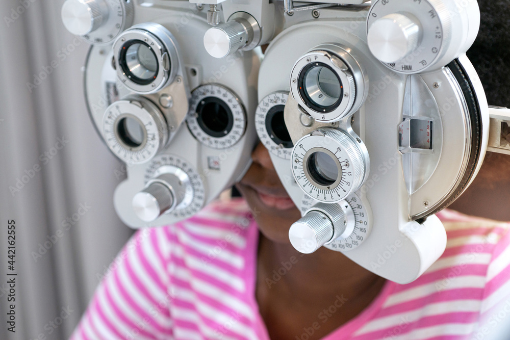 Dark skinned girl looking through optical Phoropter during eye exam, diagnostic ophthalmology equipment, selective focus Dark skinned girl looking through optical Phoropter during eye exam, diagnostic ophthalmology equipment, selective focus