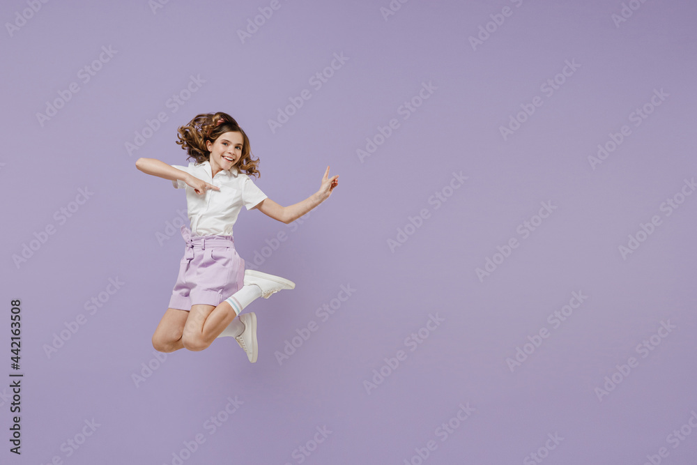 Full length smiling little kid girl 12-13 years old wear white shirt jump high point index finger aside on workspace area mock up isolated on purple background. Childhood children lifestyle concept