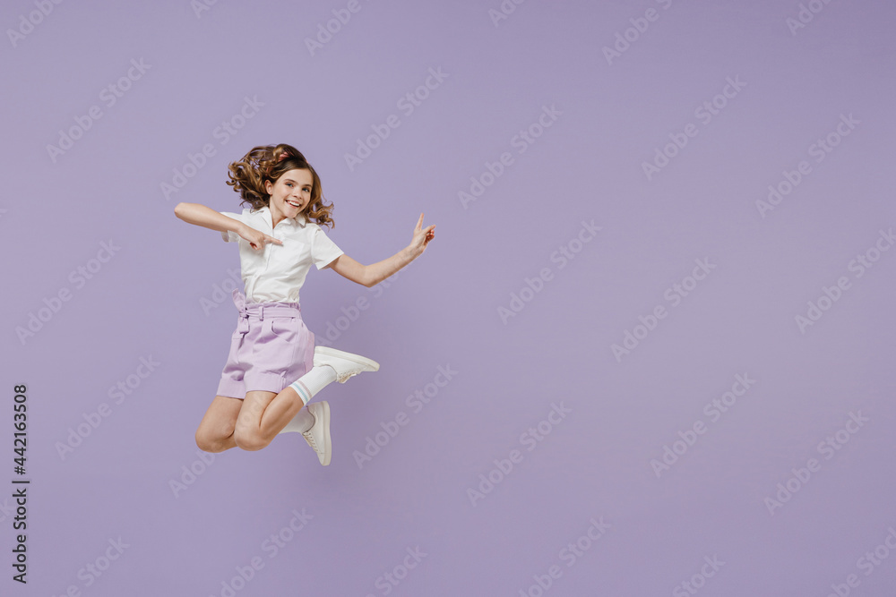 Full length smiling little kid girl 12-13 years old wear white shirt jump high point index finger aside on workspace area mock up isolated on purple background. Childhood children lifestyle concept Full length smiling little kid girl 12-13 years old wear white shirt jump high point index finger aside on workspace area mock up isolated on purple background. Childhood children lifestyle concept