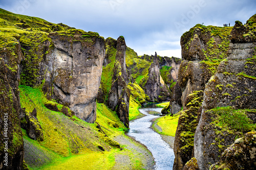 Landscape view of canyon in Fjadrargljufur, Iceland with large cliffs, river water and lush green moss grass on cloudy day