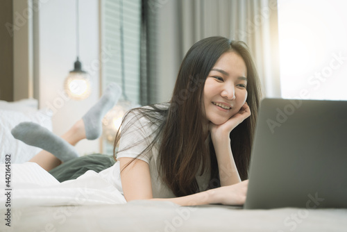 happy Young asian woman working with laptop in bed at home in the morning. lifestyle concept