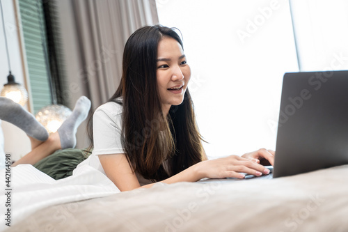 happy Young asian woman working with laptop in bed at home in the morning. lifestyle concept