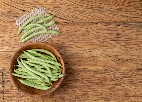 A group of green bean pods in a bowl over wooden table with copy space