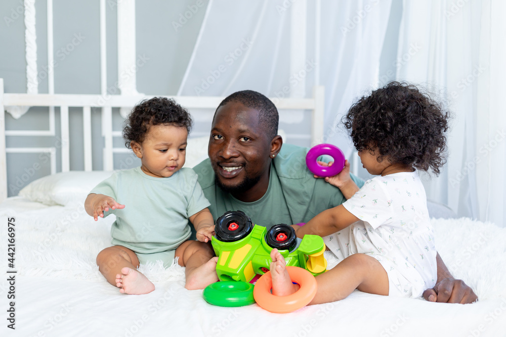 african-American family dad with kids babies play and collect a colorful pyramid at home on the bed, happy family