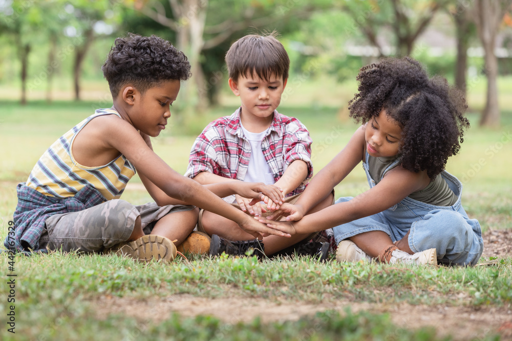 Multi-ethnic children in casual clothing sitting on green grass at the park join hands together,student tour is a good experience.