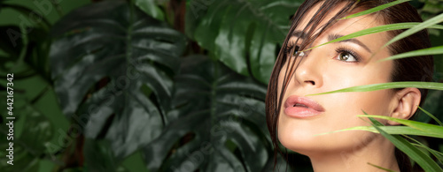 Beauty and skin care concept with a beautiful woman face amongst green tropical leaves. Wellness, natural beauty and skin care or spa treatments