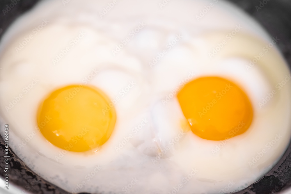 Cooked tender, soft fried eggs with two bright round raw yolks in whites with bubbles in a black frying pan. Simple breakfast. Top view, close-up. Look like eyes Cooked tender, soft fried eggs with two bright round raw yolks in whites with bubbles in a black frying pan. Simple breakfast. Top view, close-up. Look like eyes
