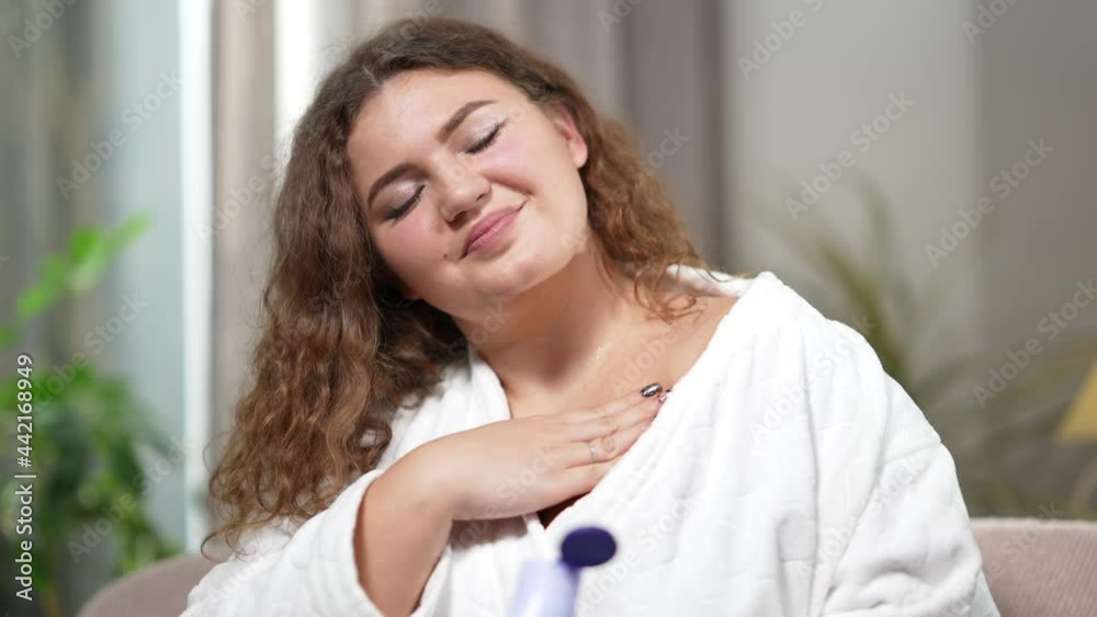 Young smiling overweight woman applying body lotion in the evening at home. Portrait of cheerful beautiful plus-size Caucasian lady in bathrobe taking care of skin indoors. Femininity and moisturizing Young smiling overweight woman applying body lotion in the evening at home. Portrait of cheerful beautiful plus-size Caucasian lady in bathrobe taking care of skin indoors. Femininity and moisturizing