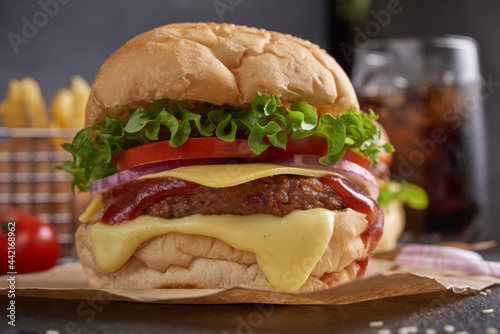 Homemade hamburger or burger with fresh vegetables and cheese lettuce and mayonnaise served  French fries on pieces of brown paper on black stone table . concept of fast food and junk food