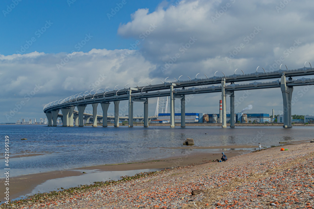 View of the rounded motorway highway bridge against a background of blue sky with clouds. The road passing over the sea bay near the coast of the city. Saint Petersburg, Europe