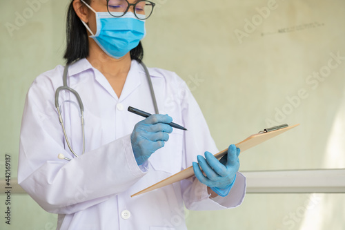 worker doctor in front of healthcare ICU facility,wearing protective PPE face mask equipment,holding medical lab patient health check form. Friendly smiling female doctor using clipboard in clinic.