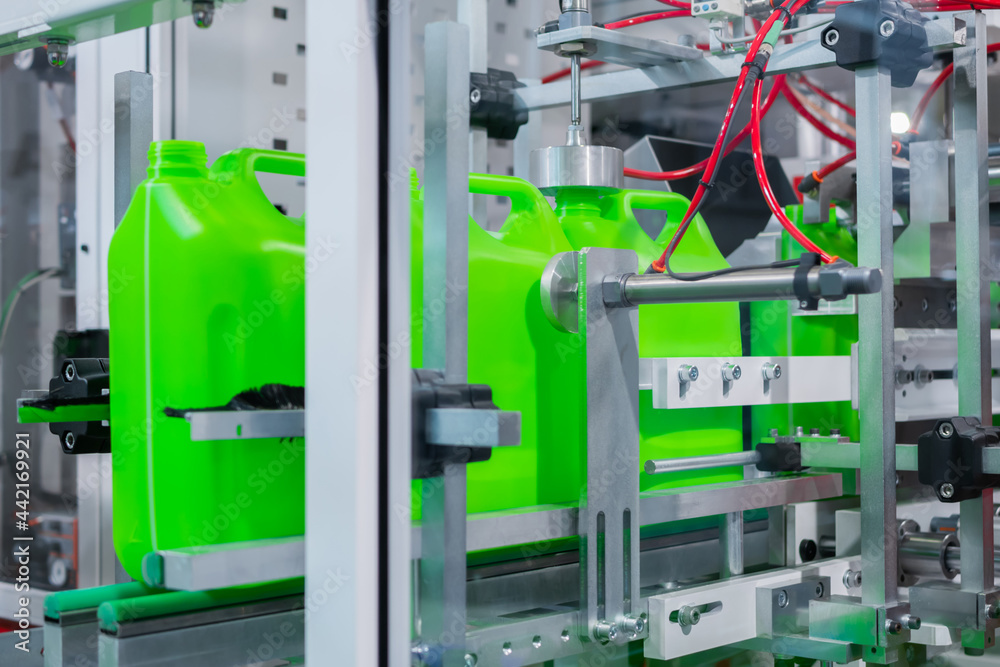 Empty green plastic jerrycans moving on conveyor belt of automatic pet blow molding machine at factory, exhibition. Manufacturing, recycling, industry, automated technology equipment concept