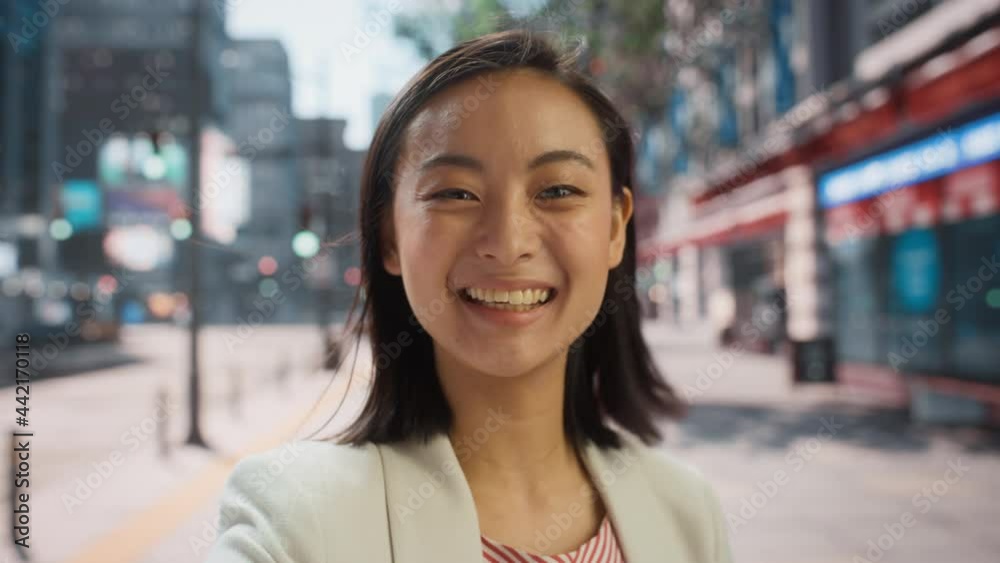 POV Video Call Portrait of a Beautiful Young Stylish Japanese Female in Smart Casual Clothes Talking to Friends or Colleagues while Standing Outside on City Street. Waving Hand in Urban Environment.
