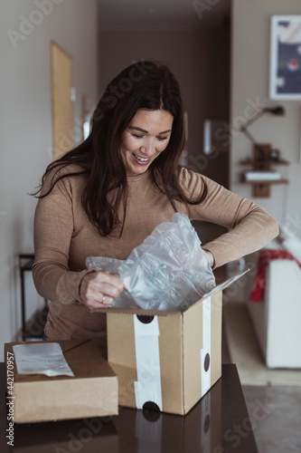 Glad kvinna öppnar paket på bänk i kök photo