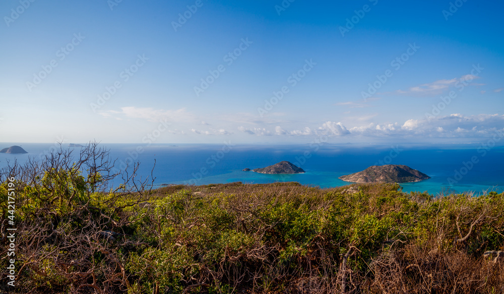A beautiful panorama from above the tropical island on the blue ocean. We meet a romantic dawn. Clear skies with a thin line of white clouds on the horizon. Two small islands can be seen in the sea.