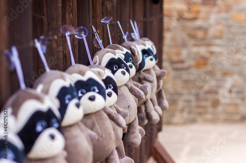 Soft raccoon toys hang in a row on a wooden background. A showcase with toys. © Alina Lebed
