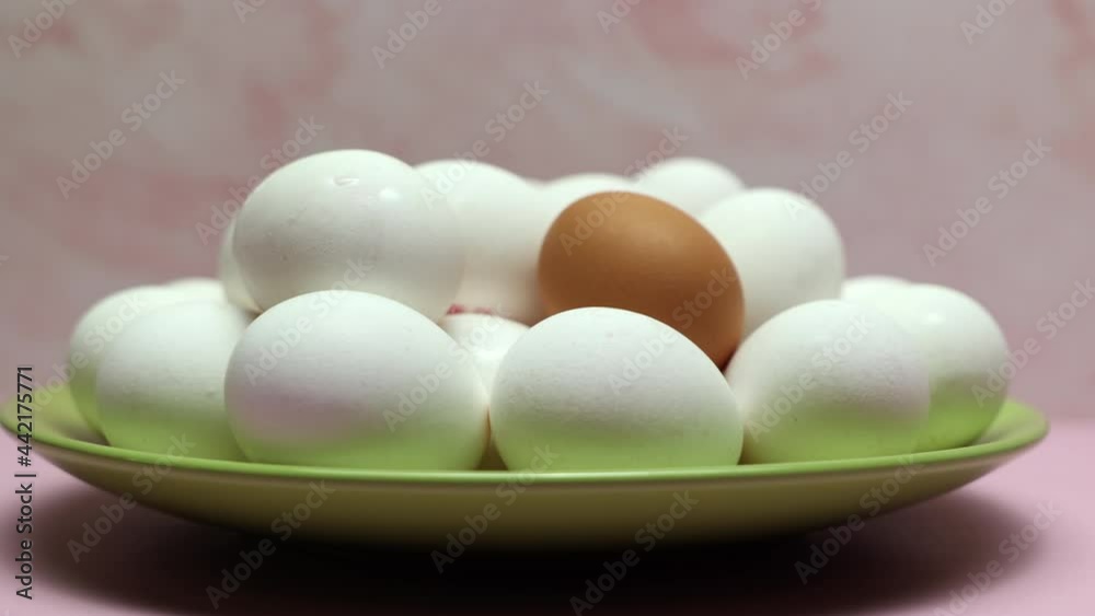 Rotating White Chicken Eggs With One Brown Egg In A Green Plate On A Pink Background. Slider Shot. Rotating White Chicken Eggs With One Brown Egg In A Green Plate On A Pink Background. Slider Shot.