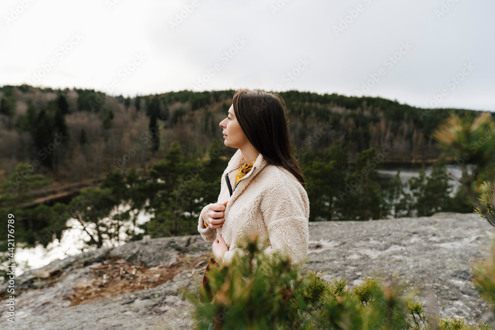 Ung kvinna står på klippa i skog och tittar bort