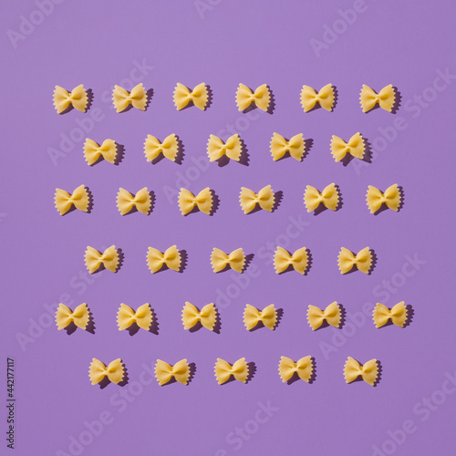Creative layout of homemade farfalle. Fun and bright food concept. Italian pasta on purple background.