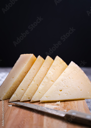 Vertical shot of triangle pieces of cured Manchego cheese and a sharp knife on a wooden food board photo