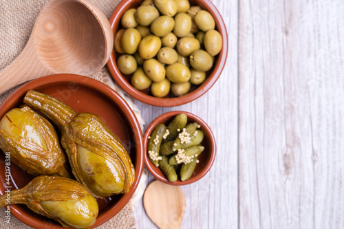 Top view of green seasoned olives, Almagro aubergine and pickles in vinegar in red bowls photo