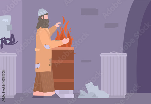 Poor dirty homeless beggar in torn clothes heating hands near barrel with fire