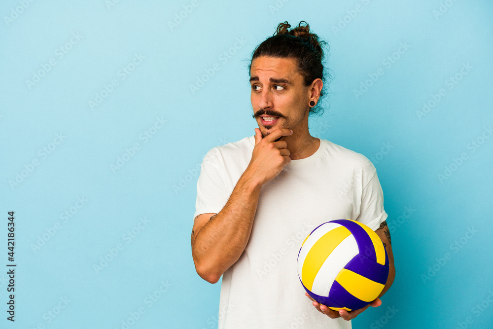 Young caucasian man with long hair isolated on blue background relaxed thinking about something looking at a copy space.