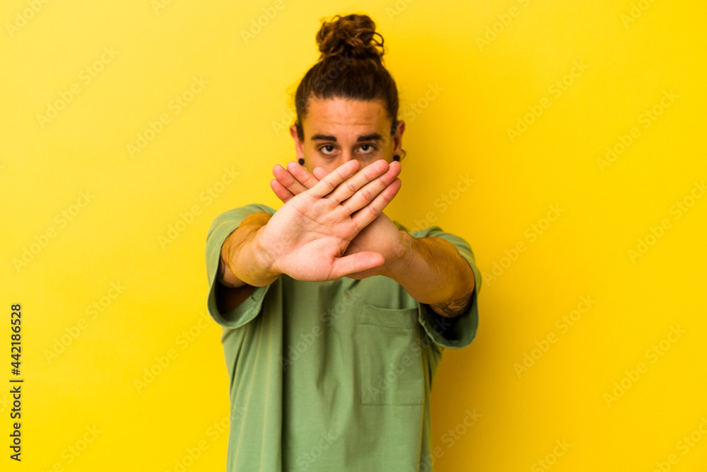 Young caucasian man with long hair isolated on yellow background doing a denial gesture