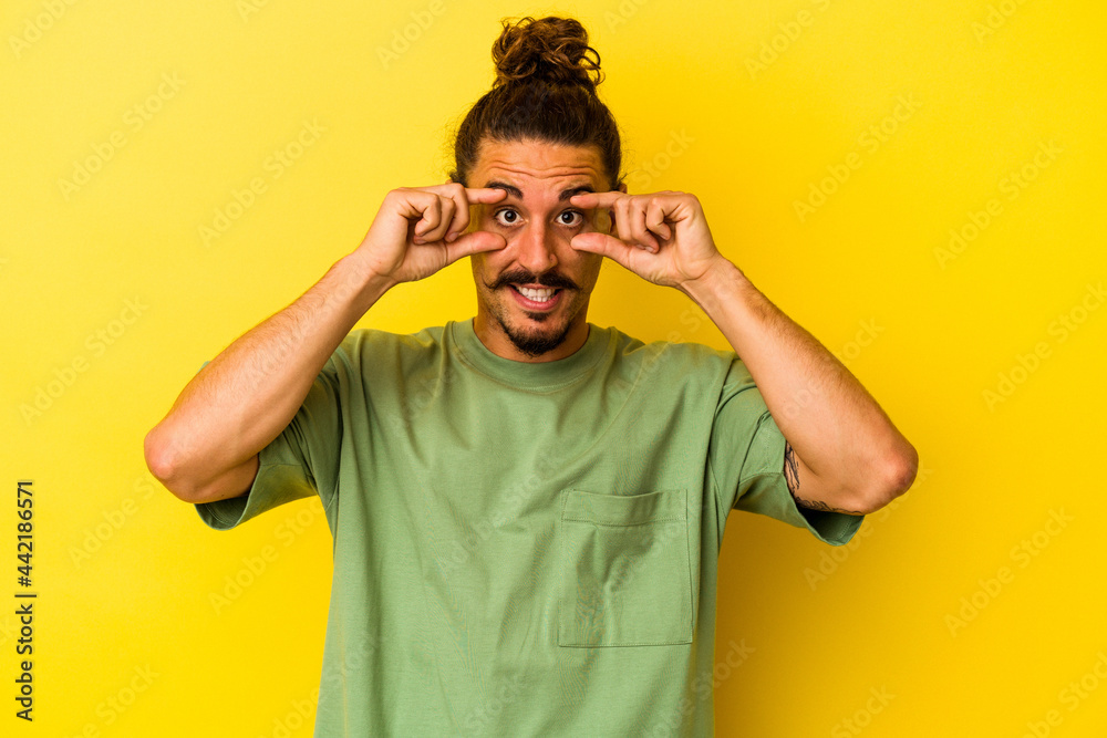Fototapeta premium Young caucasian man with long hair isolated on yellow background keeping eyes opened to find a success opportunity.