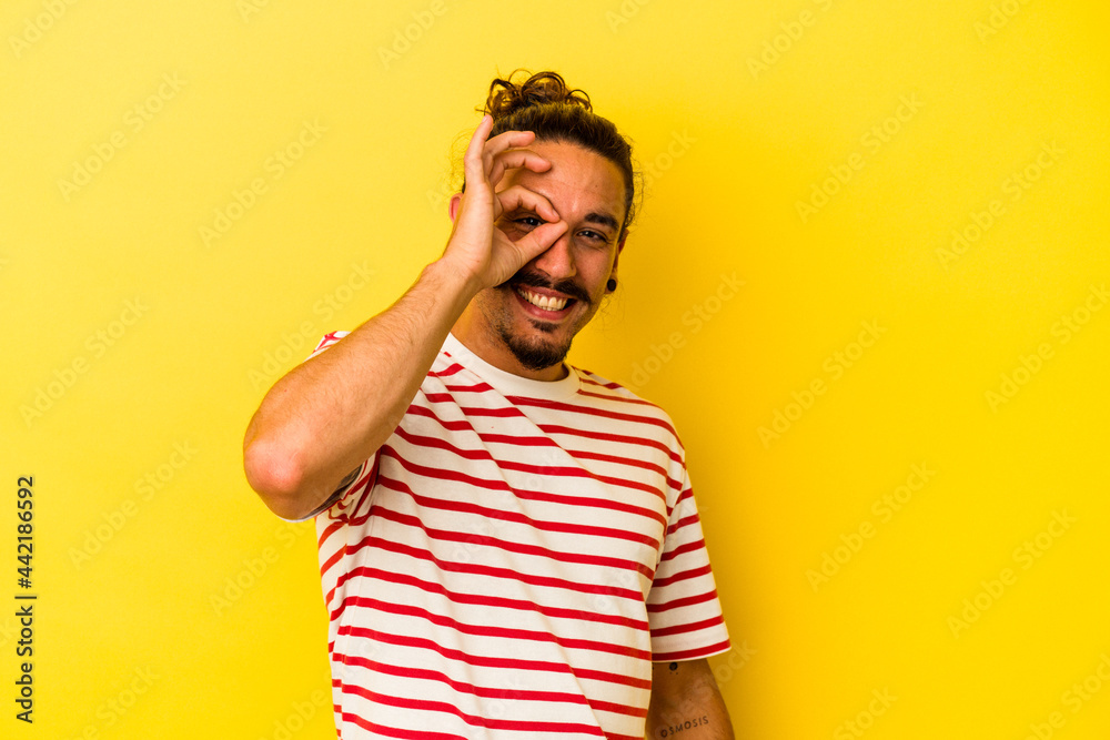 Young caucasian man with long hair isolated on yellow background excited keeping ok gesture on eye. Young caucasian man with long hair isolated on yellow background excited keeping ok gesture on eye.