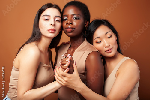 young pretty caucasian, afro, asian, scandinavian woman posing cheerful together on brown background, lifestyle diverse nationality people concept