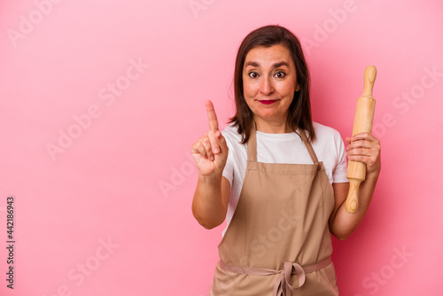Middle age pastry chef woman isolated on pink background showing number one with finger.